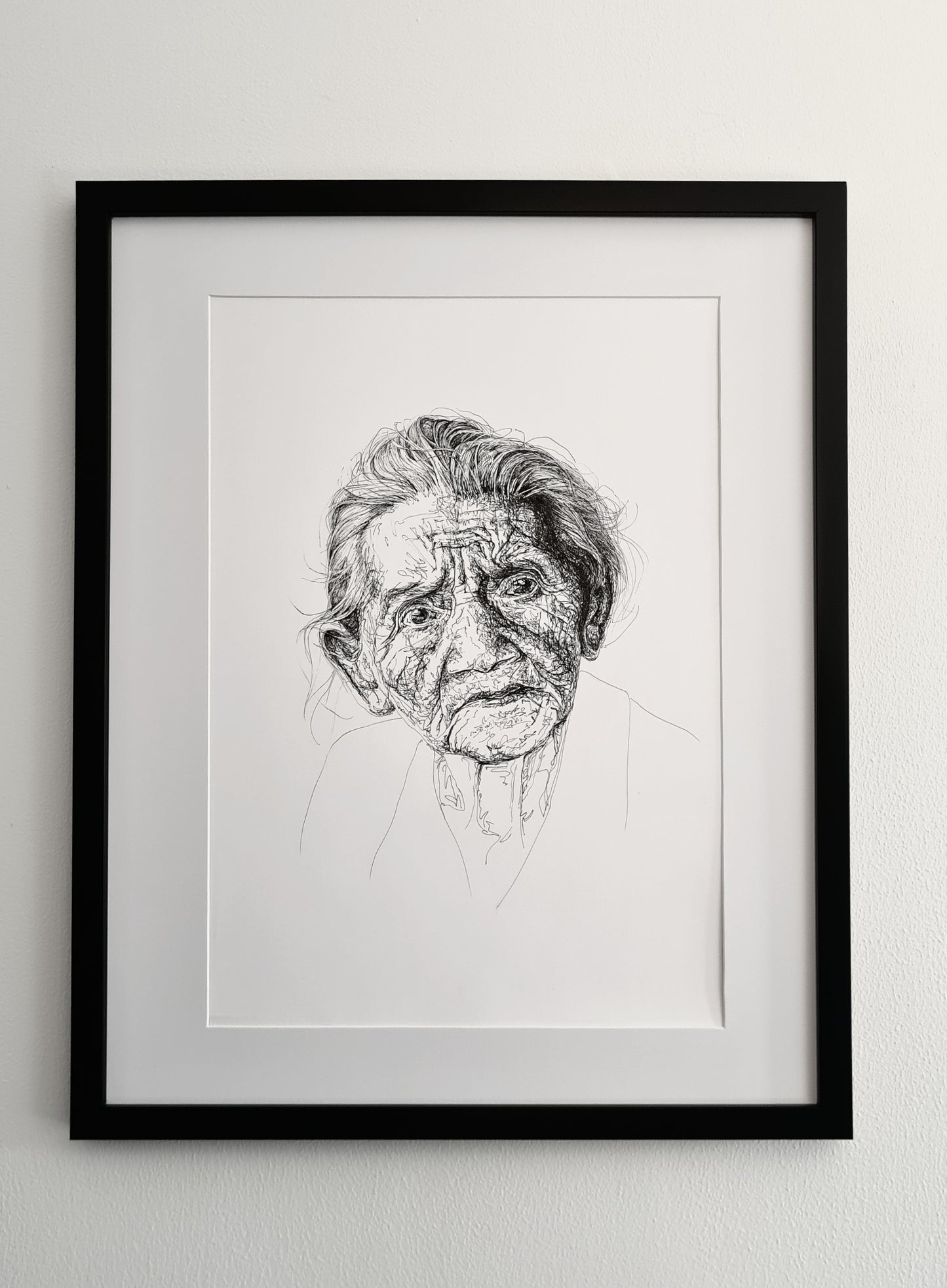 Framed and mounted black and white line drawing of an elderly person's face, hanging on a white wall