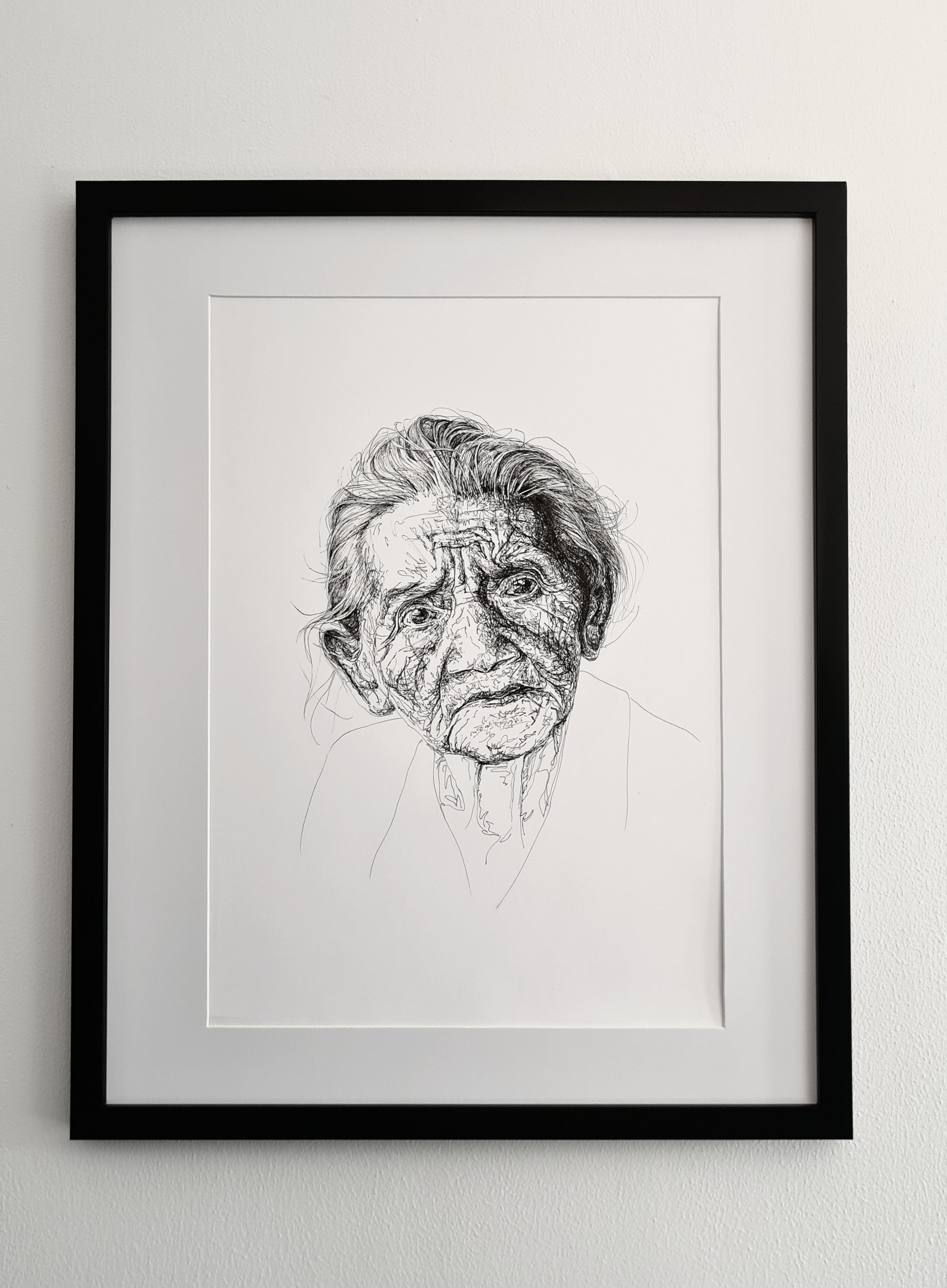 Framed and mounted black and white line drawing of an elderly person's face, hanging on a white wall